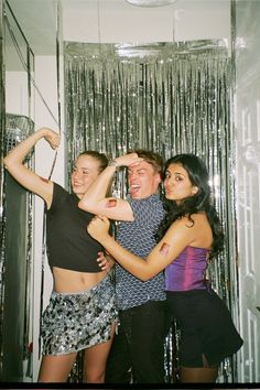 three young people posing for a photo in front of tinsel foil curtained backdrop