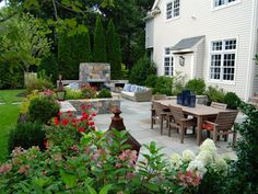 an outdoor dining area in the middle of a garden with flowers and trees around it