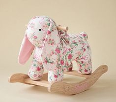 a pink and white stuffed animal sitting on top of a wooden rocking horse with floral print