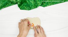 someone cutting out a paper skeleton on top of a white bed with green leaves behind it