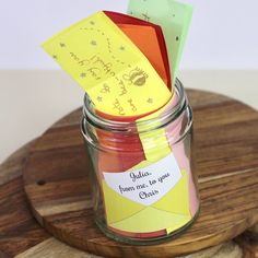 a jar filled with colorful paper on top of a wooden table next to a sign