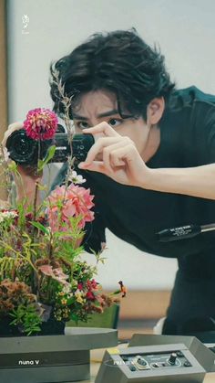 a man taking a picture of flowers with a camera in front of him on a table