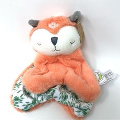 an orange stuffed animal laying on top of a white table next to a green leafy cloth