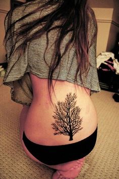 a woman's back with a tree tattoo on her lower side ribcage