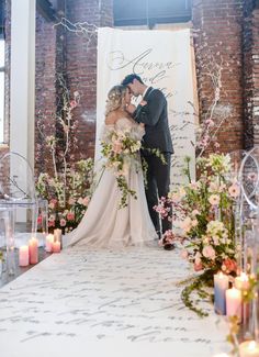 a bride and groom standing in front of a wedding sign with candles on the floor