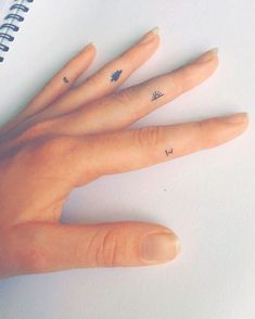 a woman's hand with two small tattoos on her left thumb and one finger