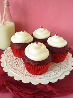 red hot velvet cupcakes with white frosting on a plate next to a bottle of milk