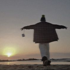 a man standing on top of a sandy beach next to the ocean with his arms outstretched