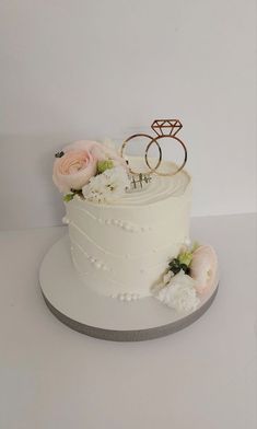 two wedding rings on top of a white cake with pink and white flowers around it