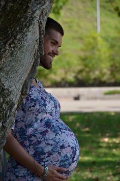 a pregnant woman standing next to a tree