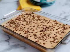 a glass baking dish filled with food on top of a marble countertop next to plates and yellow napkins