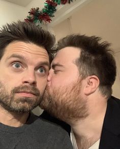 two men kissing each other in front of a christmas tree