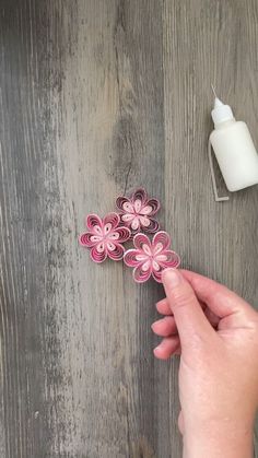 someone is holding some paper flowers on a wooden table next to a bottle of milk