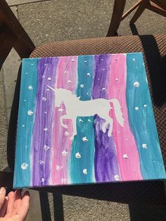 someone is holding up a painted canvas with a unicorn on it