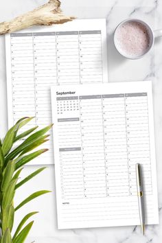 two calendars on top of a table next to a cup of coffee and a plant