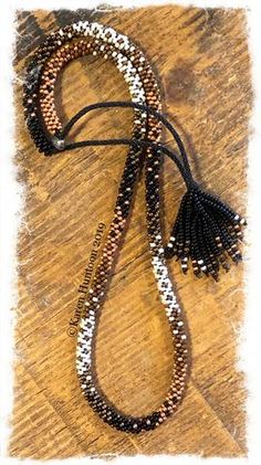 the beaded necklace is laying on top of a wooden table with a black tassel