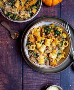 two bowls filled with pasta and vegetables on top of a wooden table next to silverware