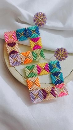 a pair of colorful beaded earrings sitting on top of a white cloth covered table