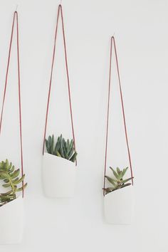 three hanging planters with plants in them against a white wall and one has a red string