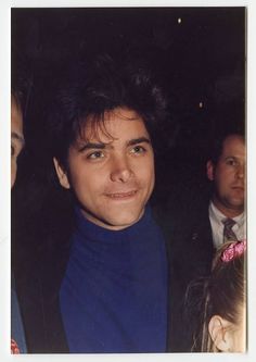 a young man in a blue turtle neck sweater standing next to other people at an event