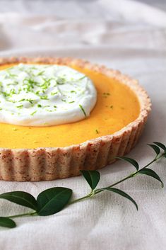 a tart with whipped cream and green leaves on the side sitting on a white cloth