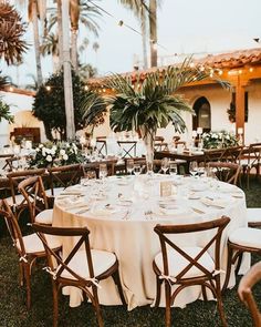 a table set up with white linens and greenery for an outdoor wedding reception