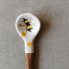 a white and yellow spoon with a bee painted on the side sitting on a gray surface