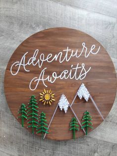 a wooden sign that says adventure awaits with pine trees and mountains on the side