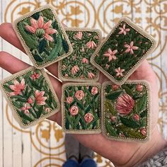 a hand holding six embroidered coasters with flowers on them and green leaves in the middle