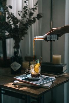 a person pouring something into a glass on top of a wooden table next to a potted plant