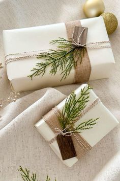 two wrapped presents are sitting on a white tablecloth with christmas decorations and baubles