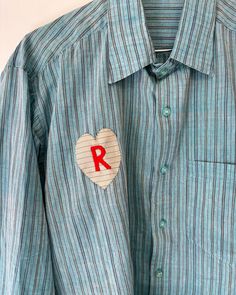 a blue shirt with a red letter on it and a heart patch in the pocket