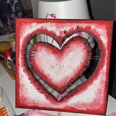 a red and white painting with a heart on it's side, surrounded by other items