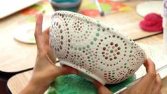 a person holding a green ball in their hands while sitting at a table with craft supplies