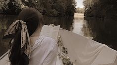 a woman is sitting in a boat on the water reading a book and looking out at the trees