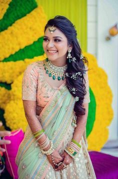 a woman in a green and white sari with jewelry on her neck, standing next to yellow flowers