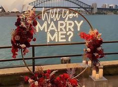 a sign that says will you marry me? with flowers and candles in front of the water