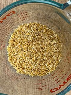 a glass bowl filled with brown rice on top of a wooden table next to a measuring cup