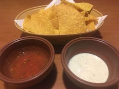 three bowls filled with salsa, tortilla chips and dipping sauce on a table