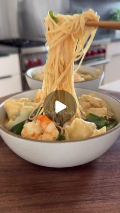 a bowl filled with noodles and shrimp being lifted by chopsticks from the bowl