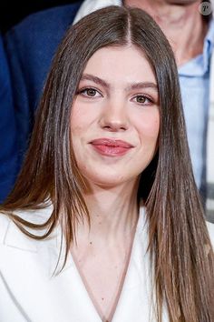 a close up of a person wearing a white shirt and long brown hair with people in the background