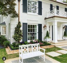 a white bench sitting in front of a house with black shutters on the windows