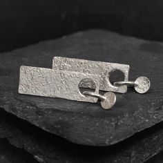 These sterling silver dangle stud earrings have a lovely organic feel to them. Length is approximately 42mm and about 10mm wide. They make quite a statement and yet minimalist.  I cut the rectangles from a textured silver sheet. I then cut the discs from the rectangles and make two small jump rings to solder them onto.  I love the way the discs are like charms on the sheet studs. The combination of stud and dangle makes them interesting, I really like them. A great length and eye catching. You can find more of our Studs and Dangles here: https://www.etsy.com/uk/shop/MikAndMandi?ref=search_shop_redirect&section_id=31890834 All our pieces are individually made, and no two will be exactly the same. We cherish these differences, and we hope you do too ;D Silver Hammered Rectangular Earrings, Minimalist Hammered Silver Earrings, Minimalist Silver Hammered Earrings, Modern Hammered Rectangular Earrings, Silver Minimalist Dangle Plug Earrings, Handmade Minimalist Silver Plug Earrings, Minimalist Handmade Silver Plug Earrings, Handmade Modern Silver Plug Earrings, Modern Handmade Silver Plug Earrings