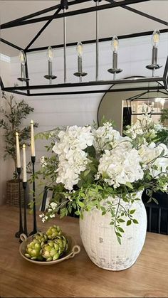 a white vase filled with flowers sitting on top of a wooden table next to a mirror