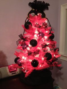 a pink christmas tree with black and white ornaments on it's top, is lit up