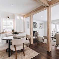 a dining room table with chairs and a clock mounted to the wall above it in front of a kitchen