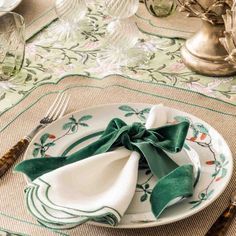 a place setting with napkins, silverware and green bows on the table cloth