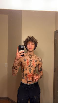 a man with tattoos taking a selfie in front of a mirror while holding a cell phone