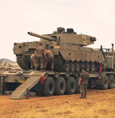 two men standing on top of a tank in the middle of a field with another man next to it