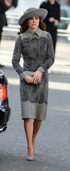 a woman in a gray dress and hat walking down the street